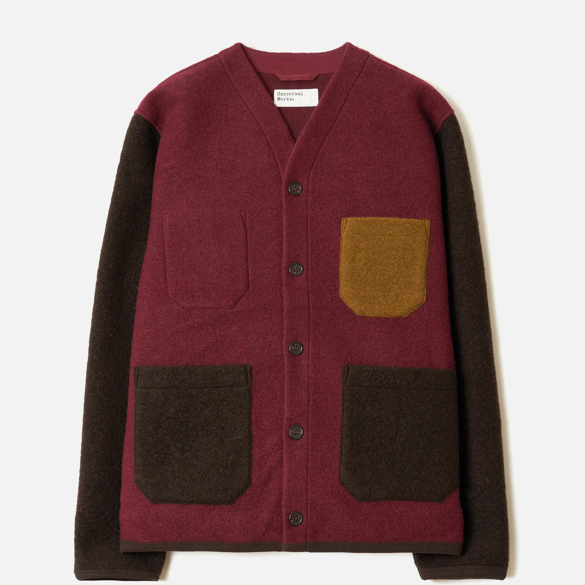 A color-block knit cardigan with a burgundy body, dark brown sleeves and front patch pockets, and a mustard yellow pocket on the chest, shown flat on a light gray background.