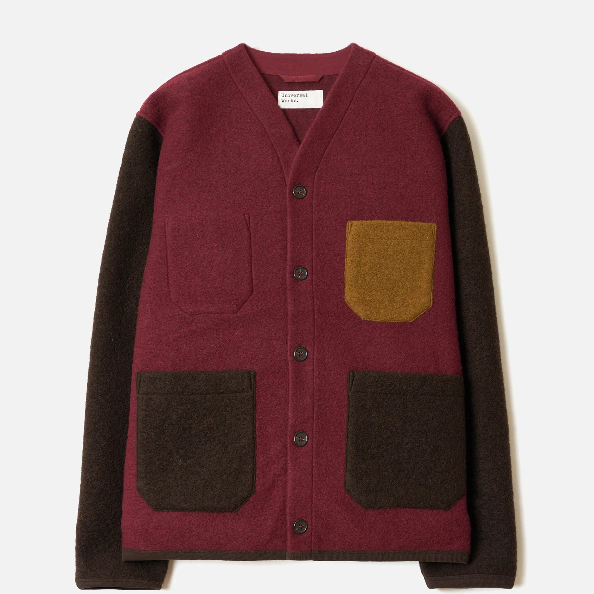 A color-block knit cardigan with a burgundy body, dark brown sleeves and front patch pockets, and a mustard yellow pocket on the chest, shown flat on a light gray background.