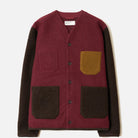 A color-block knit cardigan with a burgundy body, dark brown sleeves and front patch pockets, and a mustard yellow pocket on the chest, shown flat on a light gray background.