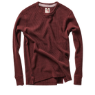 A long-sleeve crewneck knit top in a deep burgundy red, styled with a loose, draped fit and a small button detail near the hem, shown on a plain white background.