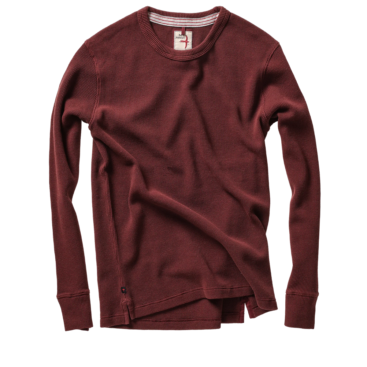 A long-sleeve crewneck knit top in a deep burgundy red, styled with a loose, draped fit and a small button detail near the hem, shown on a plain white background.